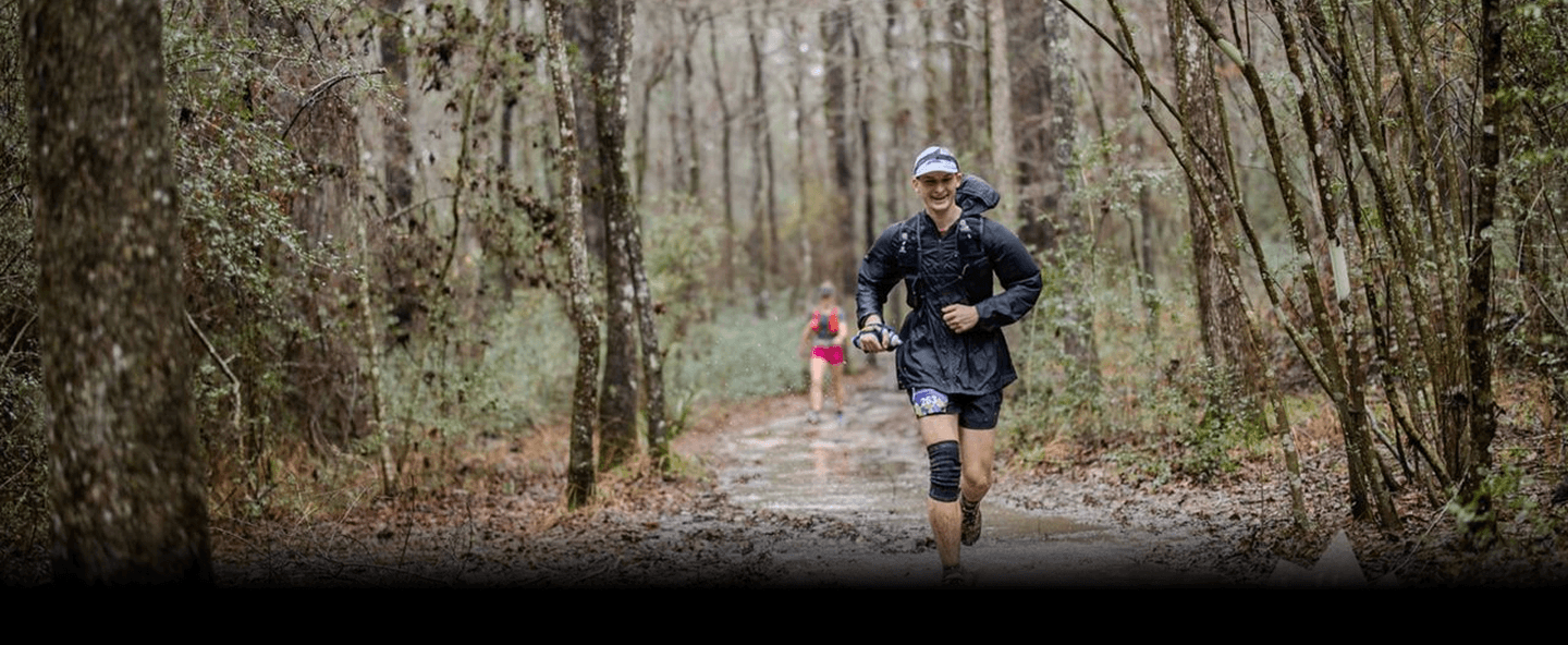 A long distance marathon runner, jogging along a wooded trail.